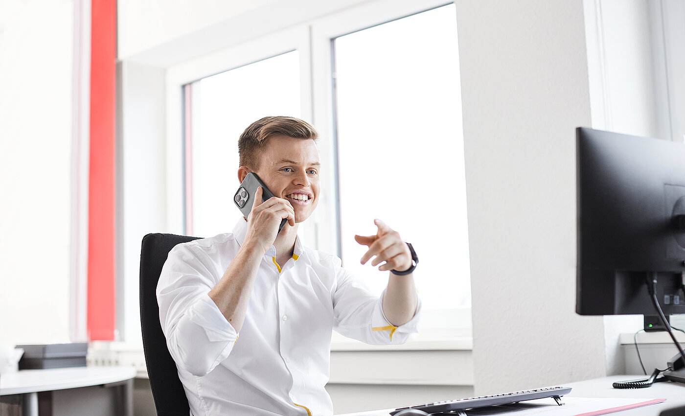 Ein lächelnder Mann. der vor seinem Computer sitzt und telefoniert