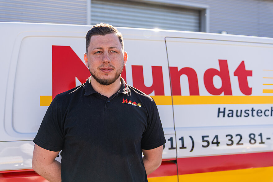 Professioneller Mitarbeiter von Mundt Haustechnik posiert vor einem gelb-roten Servicefahrzeug.