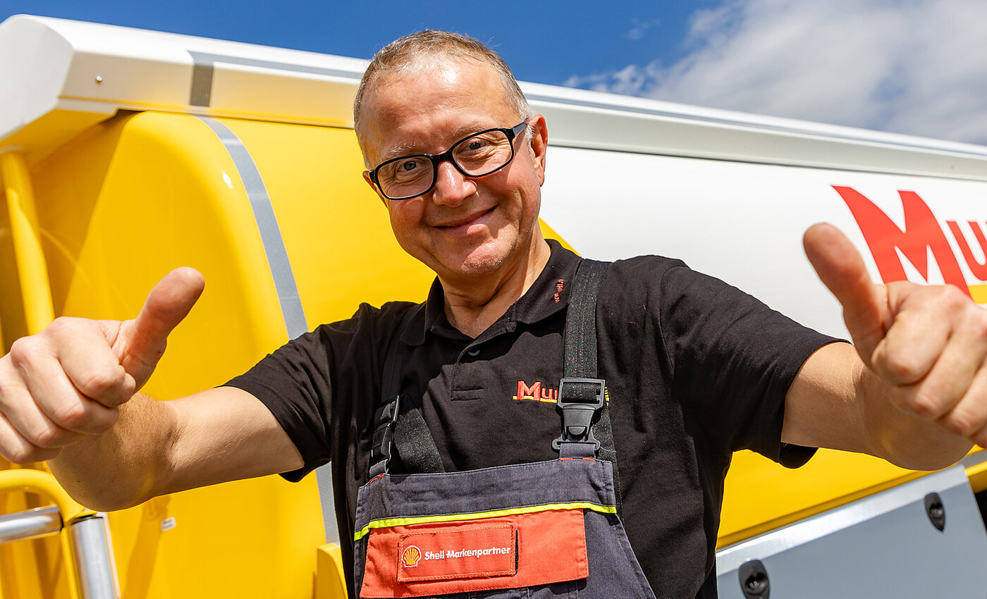 Ein lächelnder Mann der beide Daumen nach oben streckt und vor einem Mundt Tankwagen steht