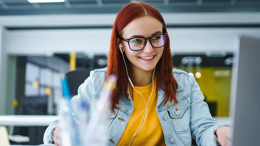 Frau sitzt mit Kopfhöhrern vor einem Computer