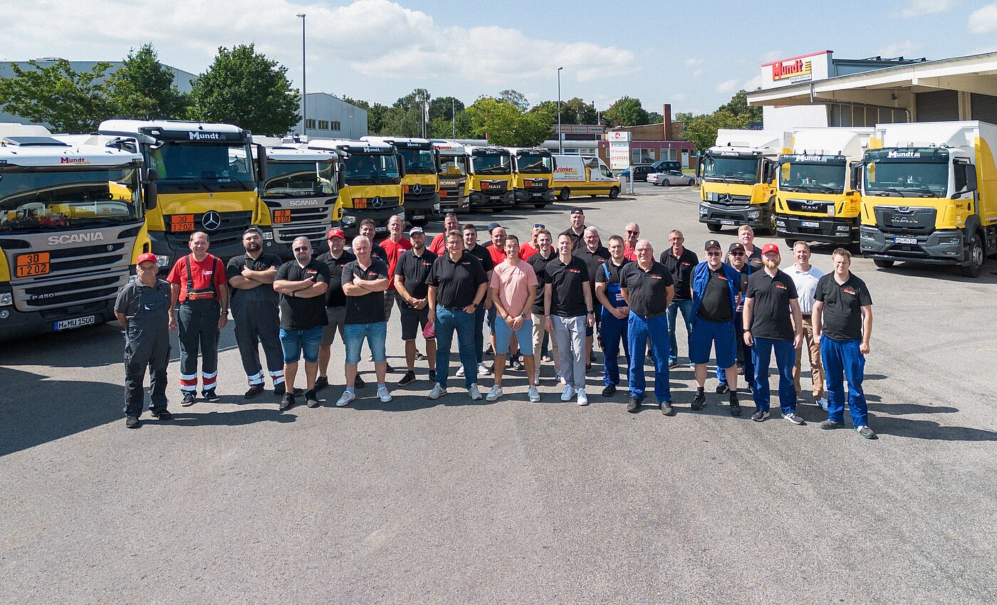 ein Gruppe von verschiedenen Personen stehen auf einem Parkplatz mit LKWs um sie herum